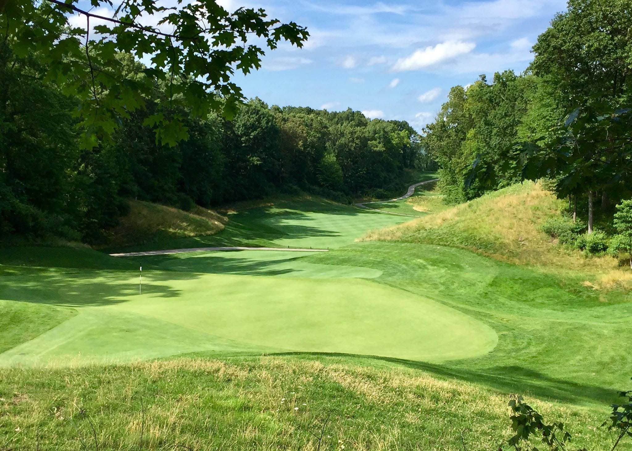 A green with the flag in, looking back down a tree-lined valley fairway